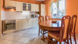 A compact kitchen with a stove, oven, and cabinets, a dining table with chairs, and a window with curtains. - Janezic apartment- Charming 2-Bedroom Apartment with Parking and grill (Baška)