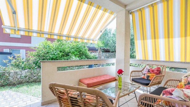 A balcony with wicker furniture, a glass table, and yellow-striped curtains. - Janezic apartment- Charming 2-Bedroom Apartment with Parking and grill (Baška)