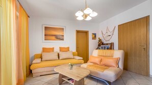 A living room with a yellow sofa, a wooden coffee table, and a white sofa. There is a wooden door and a framed picture on the wall. - Janezic apartment- Charming 2-Bedroom Apartment with Parking and grill (Baška)
