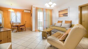 A living room with a sofa, a dining table with chairs, a coffee table, and a TV. - Janezic apartment- Charming 2-Bedroom Apartment with Parking and grill (Baška)