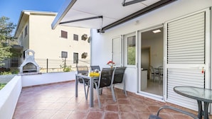 A patio with a grill, outdoor seating, and a sliding glass door leading to an interior space. - Apartment Jadranka with garden and barbeque (Baška)
