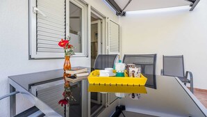 A small room with a glass table, a yellow tray with cups and a coffee maker, a vase with red flowers, and a window with white shutters. - Apartment Jadranka with garden and barbeque (Baška)