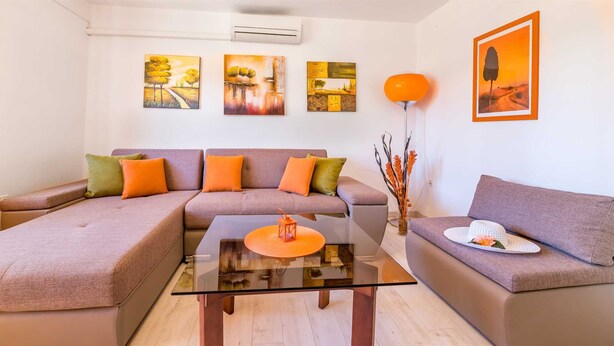 A modern living room with a sectional sofa, a glass coffee table, and a side table with a lantern. - Apartment Jadranka with garden and barbeque (Baška)