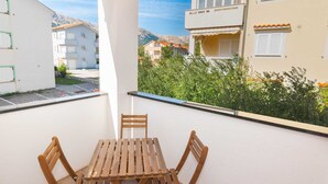 A balcony with a wooden table and chairs, overlooking a residential area with buildings and greenery. - Vera - Cozy Solo Retreat: 1BR Apartment for Two, Parking Included (Baška)