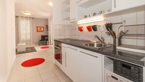 A modern kitchen with white cabinets, a black countertop, and a stainless steel sink. There are red and black mugs hanging on the wall, and a dish rack with utensils. - Vera - Cozy Solo Retreat: 1BR Apartment for Two, Parking Included (Baška)