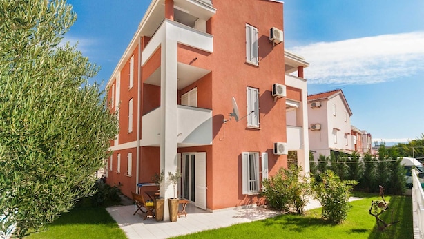 A multi-story residential building with balconies, satellite dishes, and a well-maintained garden. - Vera - Cozy Solo Retreat: 1BR Apartment for Two, Parking Included (Baška)