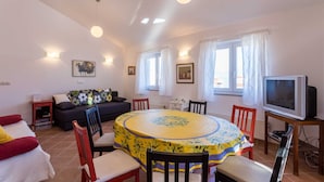 A living room with a round dining table, a sofa, a TV, and a window with curtains. - Holiday apartment Tinka in centre of Baska with seaview (Baška)
