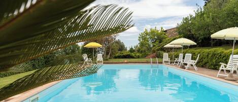 A swimming pool with white lounge chairs and yellow umbrellas, surrounded by greenery and trees.