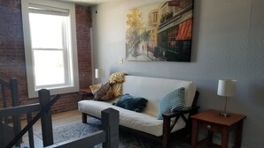 A cozy living room with a sofa, a small table, a lamp, and a painting on the wall. - Amazing Renovated Historic Loft on Main Street (Saint Charles)