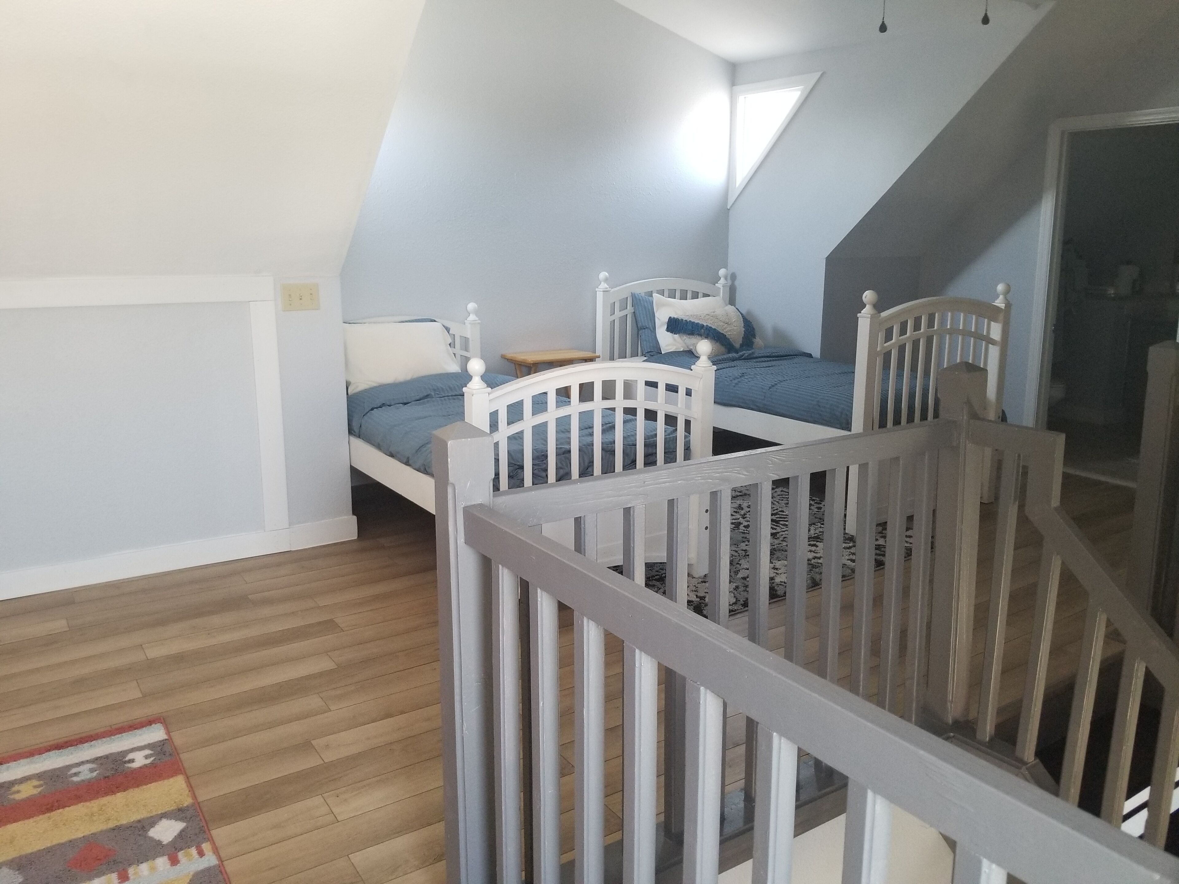 Un dormitorio con techo inclinado, dos camas individuales, suelo de madera y una mesita.