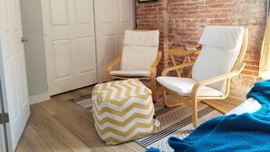 A room with a brick wall, two framed pictures, a white door, and two white chairs with wooden frames. - Amazing Renovated Historic Loft on Main Street (Saint Charles)