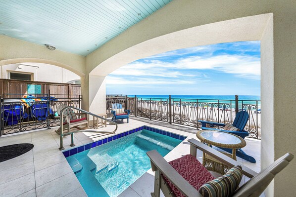 A pool area with a view of the ocean, lounge chairs, and a table.