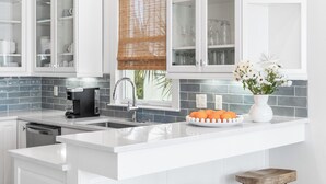 A modern kitchen with white cabinetry, a central island with stools, a coffee maker, and a decorative vase.