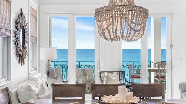 A dining area with a view of the ocean, a chandelier, and a white wall with a decorative mirror.
