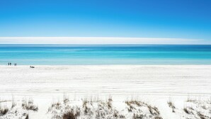 A wide sandy beach with a clear blue sky and calm sea.