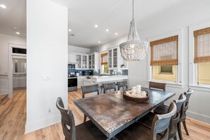 A modern kitchen with white cabinets, a central island, and a dining area with a large table and chairs.