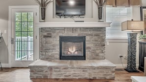 A living room with a stone fireplace, a mounted TV, and a door leading to a balcony.