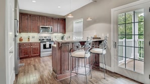 A kitchen with wooden cabinets, a central island with bar stools, a large window, and a deck visible through the door.