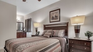 A bedroom with a large bed, two bedside tables, a dresser, a mirror, and a painting on the wall.