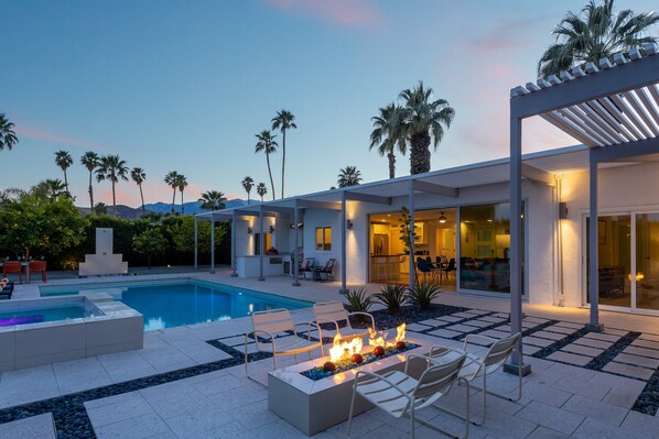 A modern outdoor pool area with a fire feature, seating, and a covered patio.