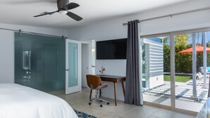 Une chambre à coucher comprenant un lit, un bureau, une chaise, un téléviseur et une porte-fenêtre coulissante donnant sur un espace extérieur.