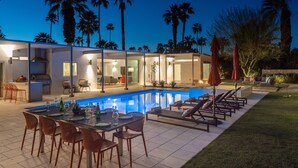 Une maison moderne dotée d’une piscine, d’un espace repas extérieur et de chaises longues.