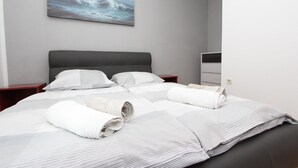 A neatly made bed with striped bedding, a gray headboard, and a painting of a seascape on the wall. - Apartments Rubil (Bale)