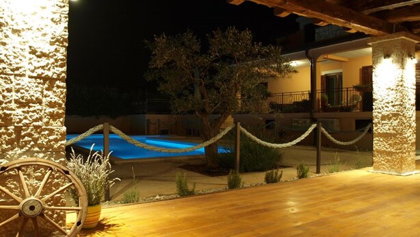A wooden deck with a rope barrier, a pool, and a building with balconies in the background. - Apartments Rubil (Bale)
