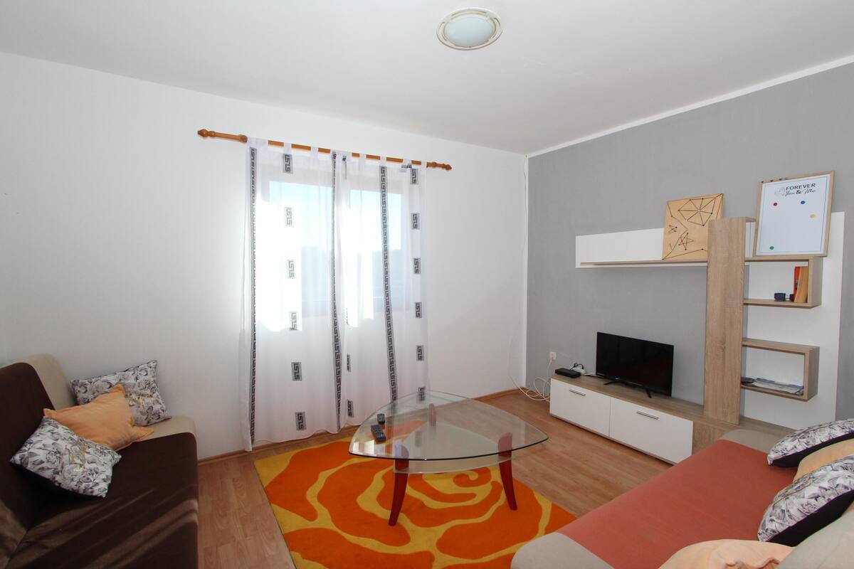 Una sala de estar moderna con una mesa de centro de vidrio, un sofá, un televisor y una estantería.