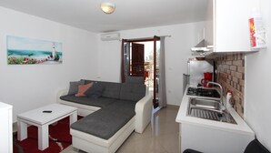 A compact living space with a sofa, a small table, a kitchen area with a sink, and a painting of a lighthouse on the wall. - Apartments Rubil (Bale)