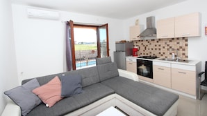 A modern living room with a grey sectional sofa, a small kitchen area with a tiled backsplash, and a view of a pool through a glass door. - Apartments Rubil (Bale)