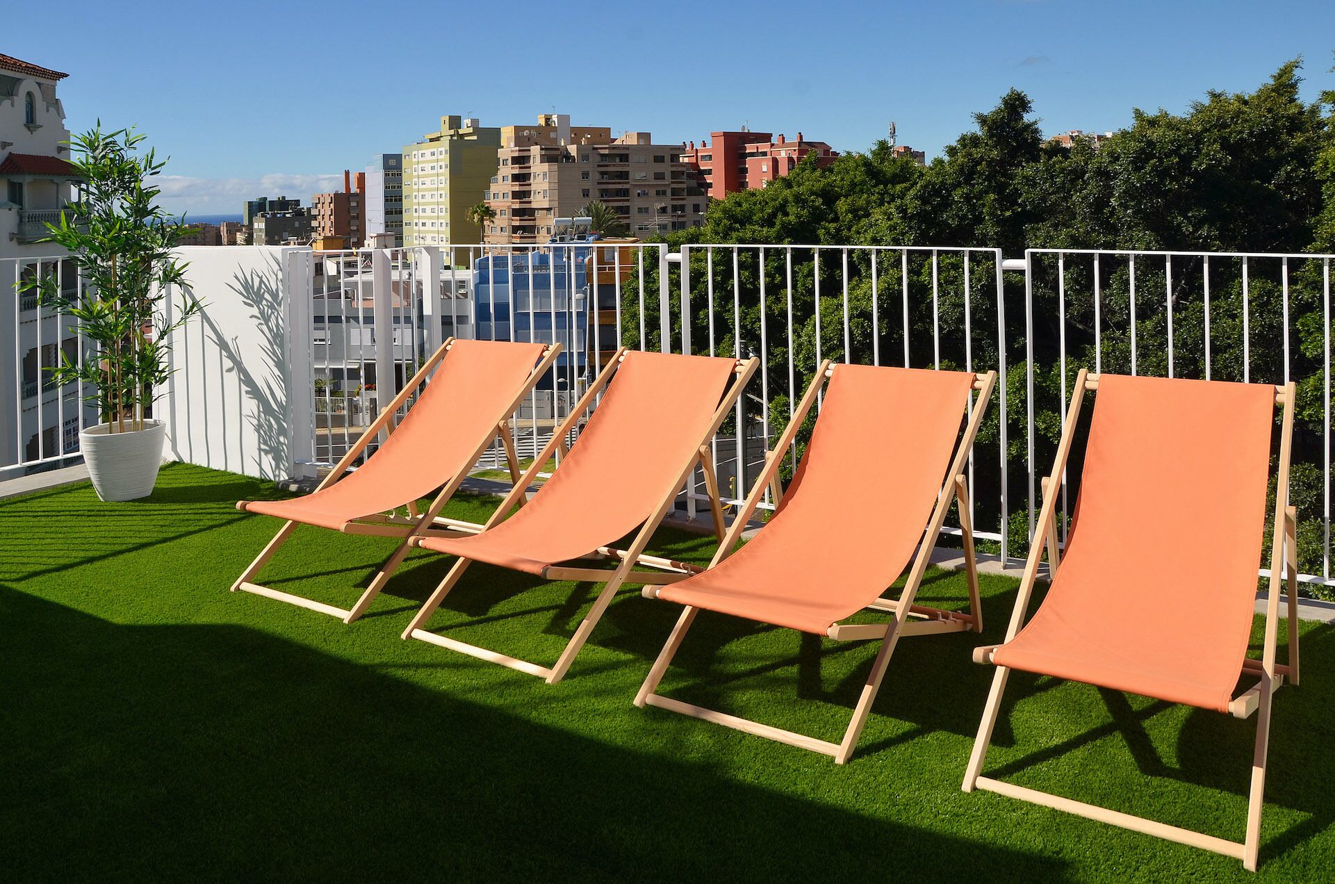 Quatre fauteuils orange sont disposés sur une pelouse verte, avec une clôture blanche et des bâtiments en arrière-plan.