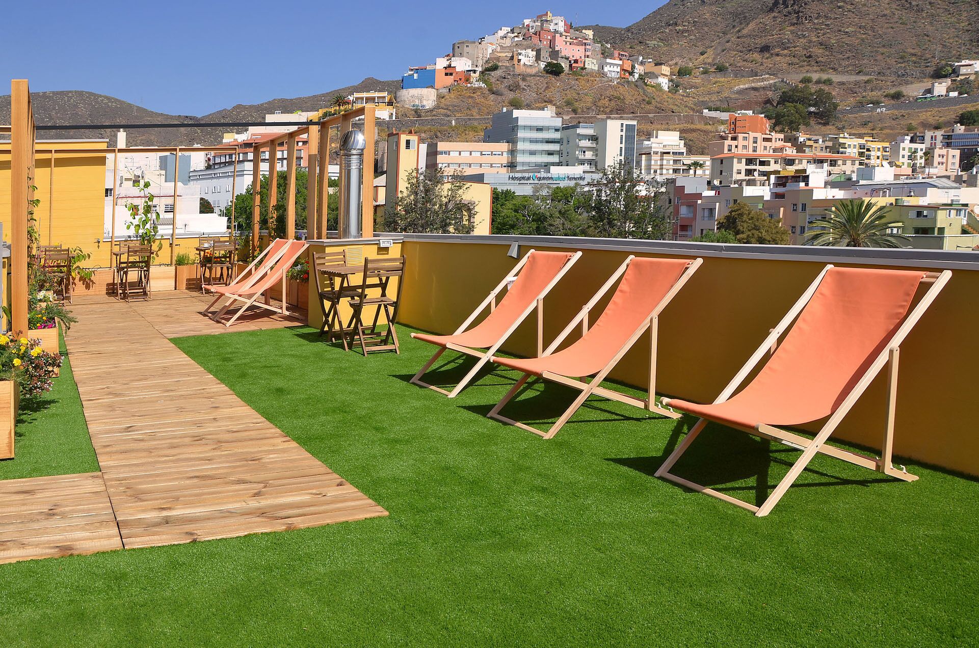 Une terrasse sur le toit avec un sol en bois et un gazon synthétique, agrémentée de fauteuils de jardin orange et d’une table en bois.