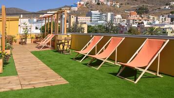 Terraza en la azotea con cubierta de madera y césped artificial, con sillas reclinables color naranja y una mesa de madera.