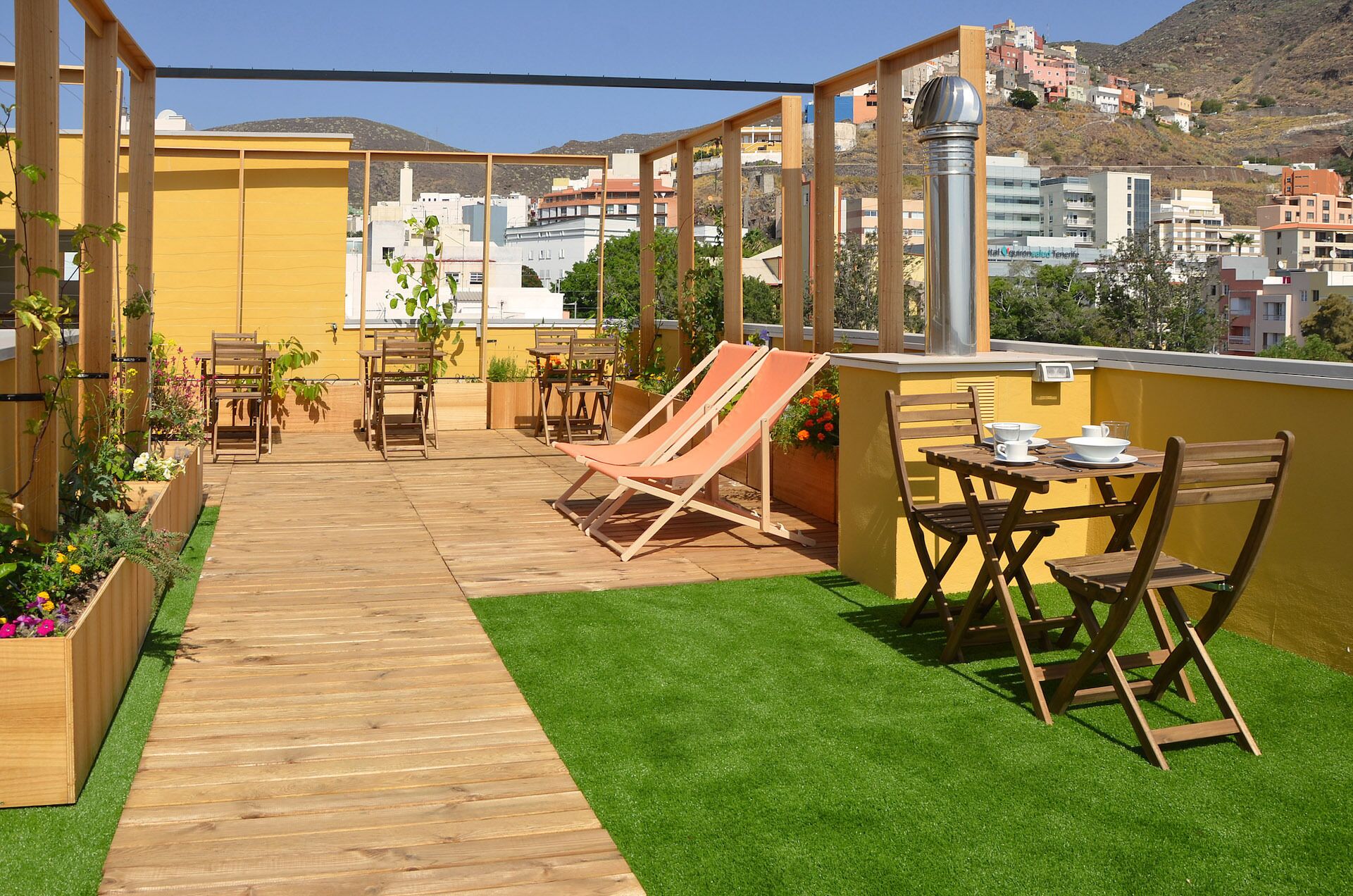 Una terraza en la azotea con mobiliario de madera, una pequeña mesa dispuesta y vistas de la ciudad.