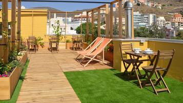 Una terraza en la azotea con mobiliario de madera, una pequeña mesa dispuesta y vistas de la ciudad.
