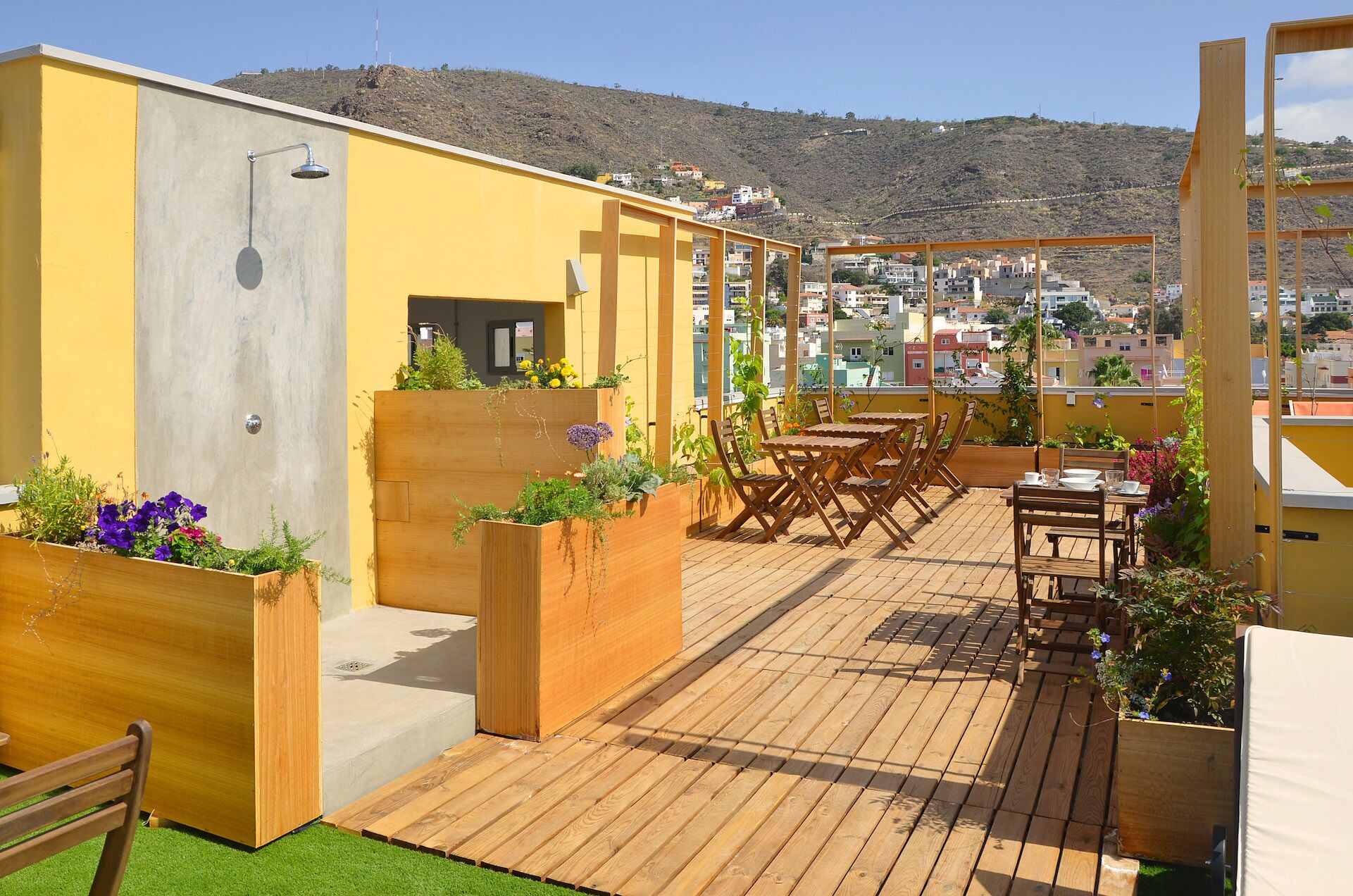 Une terrasse sur le toit, dotée d’un plancher en bois, d’une table et de chaises en bois, ainsi que de jardinières fleuries.
