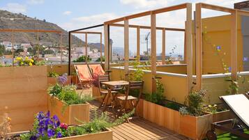 Un jardín en la azotea con terraza de madera, zona de estar y macetas elevadas con flores.