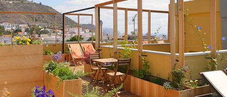 A rooftop garden with wooden deck, seating area, and raised planters with flowers.