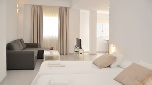 Una habitación de hotel moderna con sofá, cama con dos almohadas, una mesita con televisor y ventana con cortinas.
