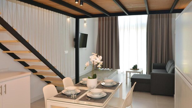 Un área de comedor moderna con una mesa de vidrio, sillas blancas y una escalera con barandillas negras.
