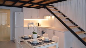 Una cocina moderna con armarios blancos, una mesa de comedor preparada para cuatro personas y una escalera con barandilla negra.