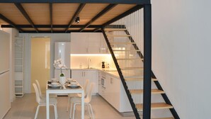 Una cocina moderna con armarios blancos, una mesa de comedor con sillas y una escalera con escalones de madera.