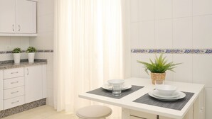Une cuisine moderne avec des armoires blanches, un comptoir en granit et une table à manger avec une chaise blanche. On trouve deux plantes en pot sur le comptoir et un panier tressé contenant une plante sur la table à manger.