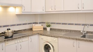 Une cuisine compacte avec des meubles blancs, un plan de travail en granit, une cuisinière, un lave-linge et un évier.