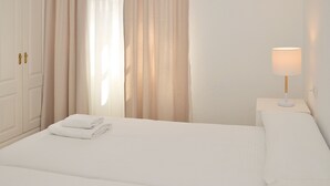 Une chambre d’hôtel avec un lit bien fait, une lampe de chevet, une fenêtre avec des rideaux et une porte dotée d’une poignée.