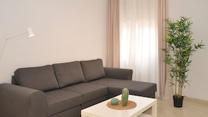 Ein graues Sofa mit Kissen, ein weißer Couchtisch mit einem Kaktus und einer dekorativen Kugel, eine Stehlampe und eine Bambuspflanze im schwarzen Topf.