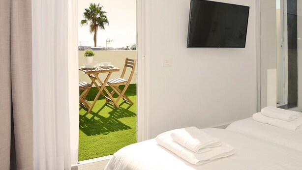 Ein Hotelzimmer mit Bett, einem an der Wand befestigten Fernseher, einem Balkon mit Tisch und Stühlen und Blick ins Freie.