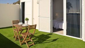 Eine Terrasse mit Holztisch und -stühlen, einem Blumentopf und einer Glastür, die zu einem Schlafzimmer mit Bett und Nachttisch führt.