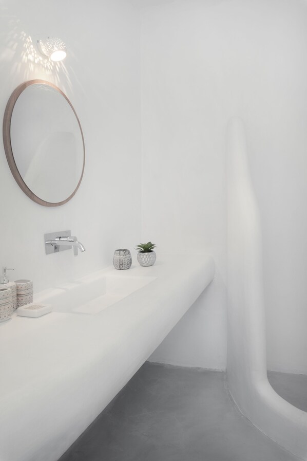 A modern bathroom with a white sink, a round mirror, and a shower with a curved design.